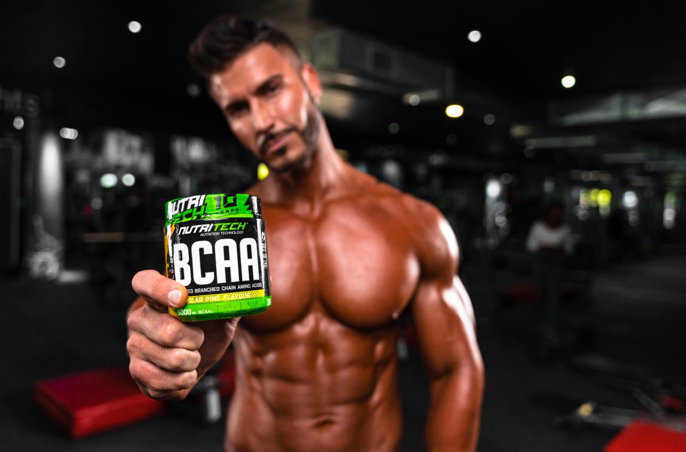 male with muscular physique holding bcaa amino acids supplement at gym
